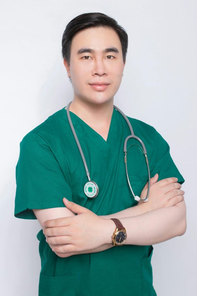 Professional portrait of a male doctor in green medical scrubs with a stethoscope.